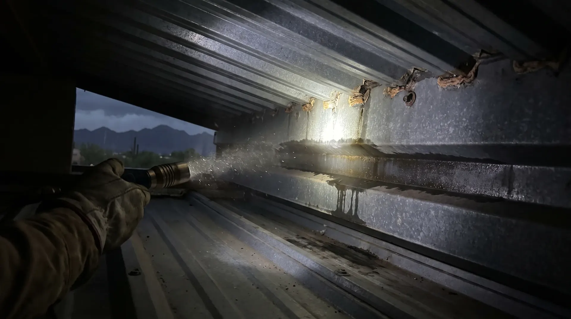 Torch beam following a water track sideways along the underside of a metal roof deck