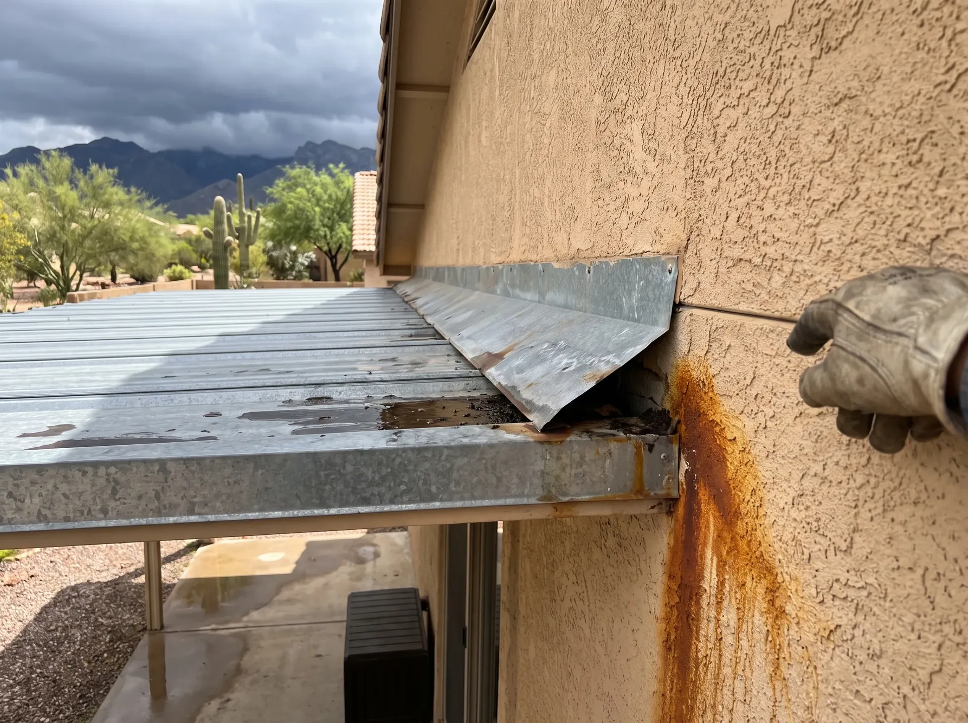 Lifted counterflashing where a metal patio cover meets a stucco wall, with rust staining below